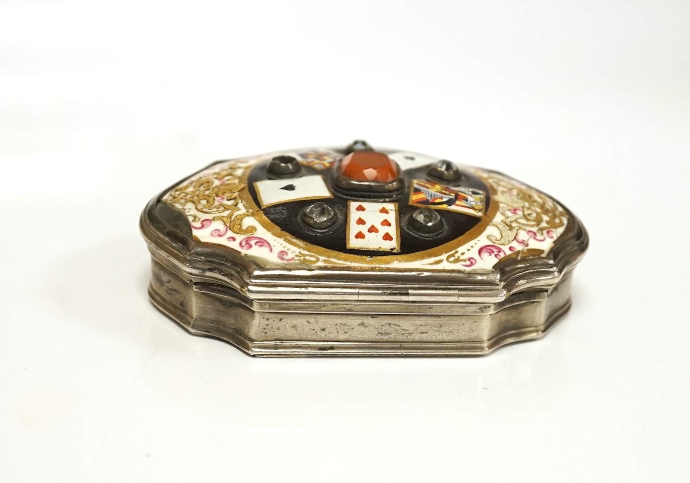 A continental white metal, enamel and two colour paste? set shaped oval snuff box, decorated with playing cards, unmarked, 67mm. Condition - poor